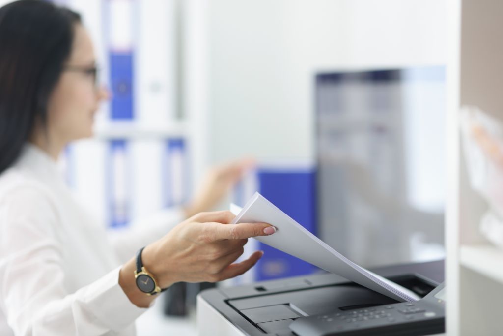 Young woman pulling paper out of printer closeup