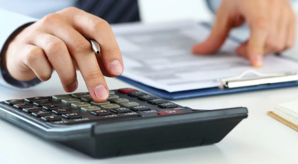 Close up view of person's hand on a calculator while reviewing paperwork