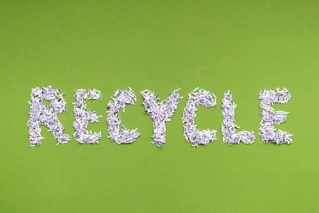 The word recycle is made from a heap of shredded white paper on green background