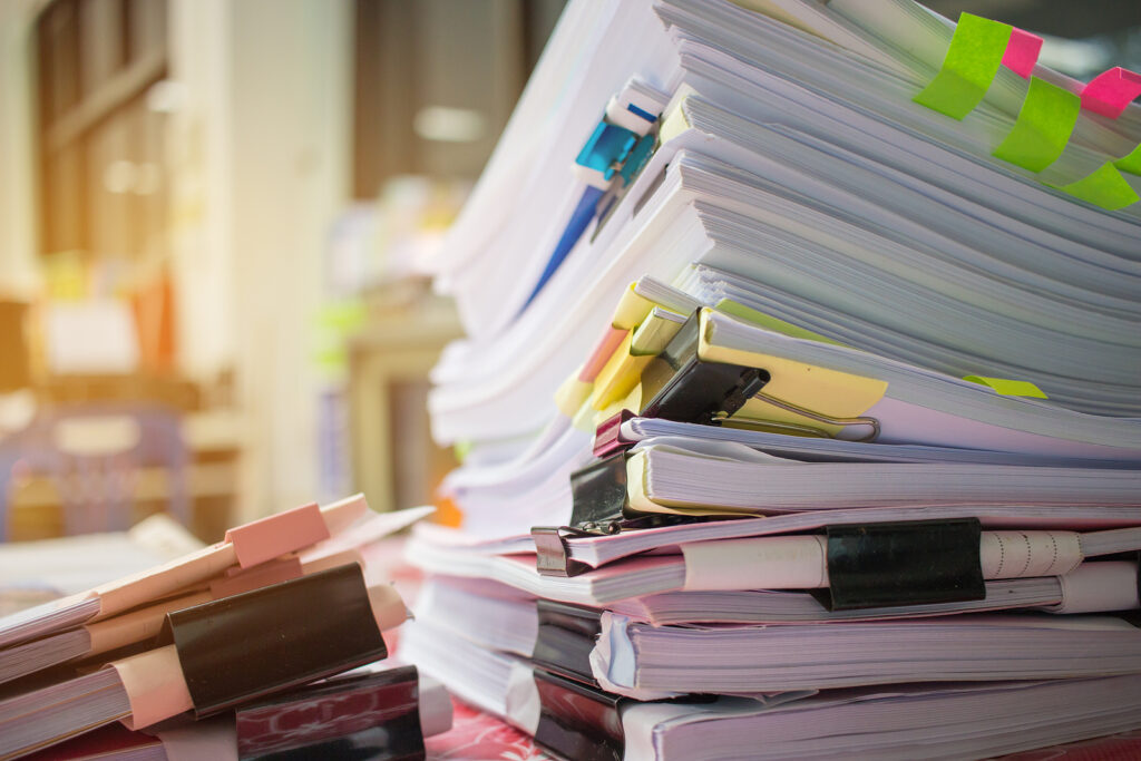 Pile of documents on office desk related to business functions.