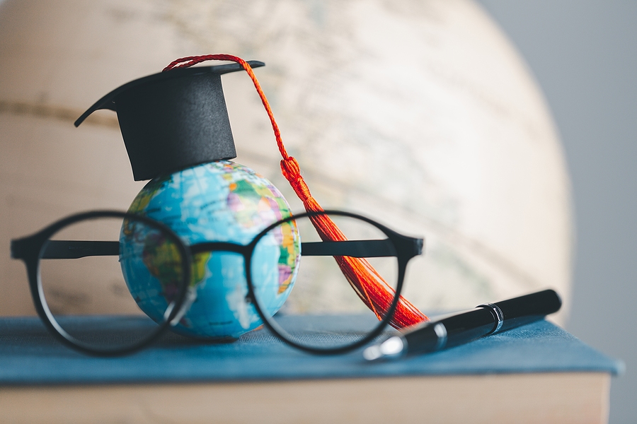 Graduation cap on a globe with eyeglasses and a pen resting on a book
